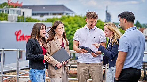 Fünf Auszubildende auf Dachterrasse mit Blick aufs Werksgelände im Hintergrund