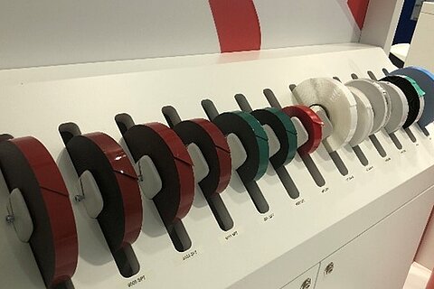 Trade show display with neatly arranged rolls of technical adhesive tapes from Coroplast Tape in various colors and configurations.