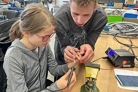 Azubi erklärt Teilnehmerin den Einsatz eines Lötkolbens