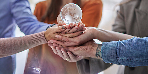 Several hands holding a glass globe