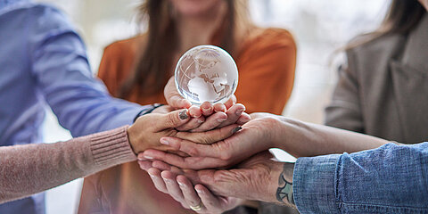 Several hands holding a glass globe